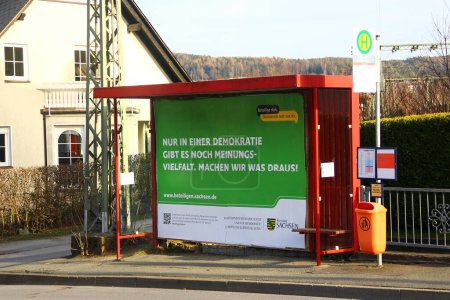 Foto de Aue-Bad Schlema, Alemania - 26 de marzo de 2024: Cartel en una parada de autobús, promoviendo la democracia e invitando a los ciudadanos a participar en programas sociales liderados por el gobierno de Sajonia - Imagen libre de derechos