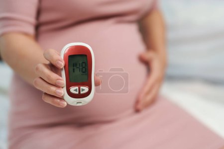 Téléchargez les photos : Gros plan de la femme enceinte tenant un glucomètre avec le résultat de la mesure du taux de sucre élevé. concept de diabète gestationnel. - en image libre de droit