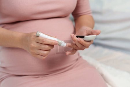Téléchargez les photos : Gros plan de la femme enceinte tenant glucomètre et vérifier le taux de sucre dans le sang par elle-même à la maison. concept de diabète gestationnel. - en image libre de droit