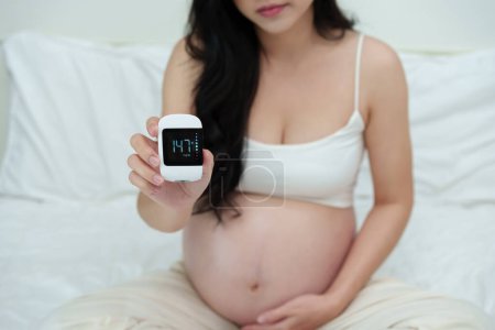 Foto de Mujer embarazada sosteniendo glucómetro con resultado de la medición de azúcar de alto nivel. concepto de diabetes gestacional. - Imagen libre de derechos