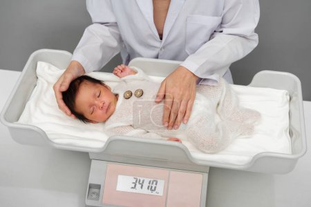 Photo for Newborn baby weight measurement on the digital scales with doctor in hospital - Royalty Free Image