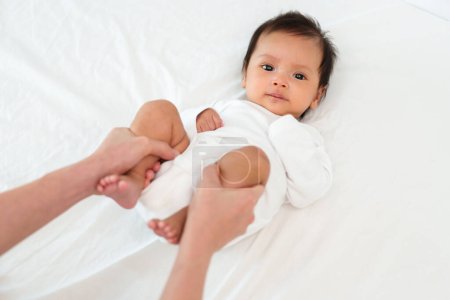 Téléchargez les photos : Les mains de la mère tenant les jambes de bébé et faisant quelques exercices ludiques sur un lit - en image libre de droit