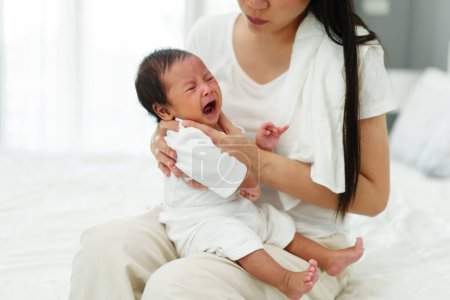 mère tenant roter et pleurer bébé dans une chambre après avoir donné du lait