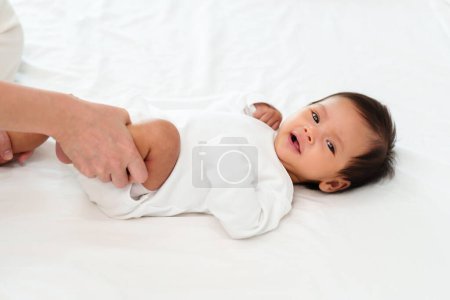 Photo for Mother's hands holding baby legs and doing some playful exercises on a bed - Royalty Free Image
