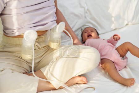 mother using breast pump machine to pumping milk with her newborn baby on a bed