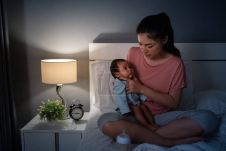 Photo for Mother holding newborn baby burping after feeding milk on a bed at night - Royalty Free Image