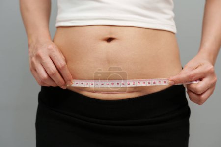 Photo for Woman using tape measuring the c-section scar of cesarean on her belly - Royalty Free Image