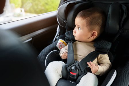 Téléchargez les photos : Bébé heureux assis dans le siège d'auto et regardant par la fenêtre, chaise de sécurité voyageant - en image libre de droit