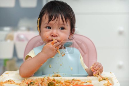 Téléchargez les photos : Bébé bébé manger des aliments et légumes en se nourrissant BLW ou bébé conduit sevrage sur une chaise - en image libre de droit