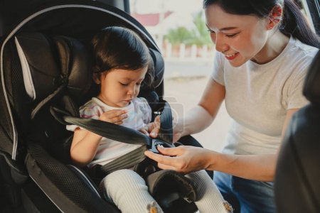 Photo for Mother is fastening safety belt to toddler girl in a car seat, safety baby chair travelling - Royalty Free Image