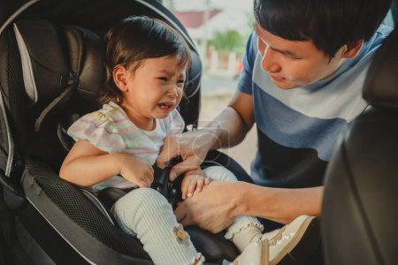 Photo for Father is fastening safety belt to crying toddler girl in a car seat, safety baby chair travelling - Royalty Free Image