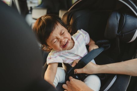 Photo for Mother is fastening safety belt to crying toddler girl in a car seat, safety baby chair travelling - Royalty Free Image