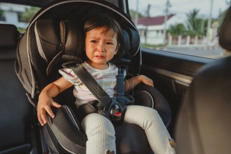 Photo for Crying toddler girl sitting in a car seat, safety baby chair travelling - Royalty Free Image