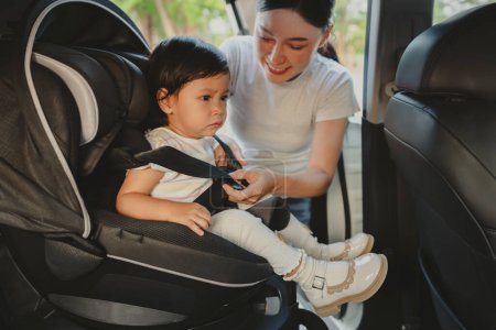 Photo for Mother is fastening safety belt to unhappy toddler girl in a car seat, safety baby chair travelling - Royalty Free Image