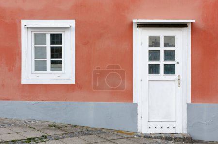 Photo for Detail of the facade of a building with the wall painted in orange and a door and a window in white - Royalty Free Image