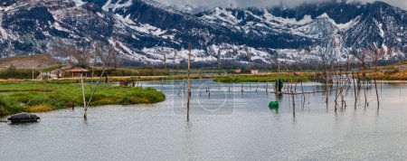varano lake where aquaculture is practiced. In the background a chain of snowy mountains produced with artificial intelligence