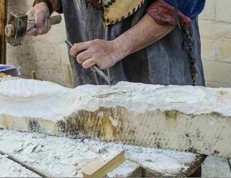 Téléchargez les photos : Reconstitution médiévale d'un tailleur de pierre façonnant la pierre avec un marteau et un ciseau - en image libre de droit