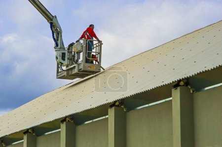 Téléchargez les photos : Les travailleurs de la construction à l'intérieur du panier de camion-grue effectuer des réparations sur le toit d'un entrepôt industriel - en image libre de droit