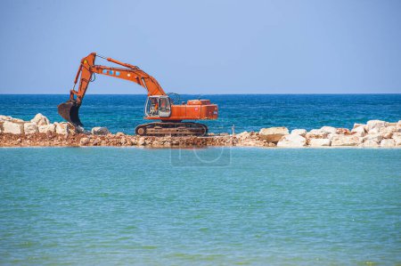 Téléchargez les photos : Excavatrice place et arrange un quai bras pour la construction du port - en image libre de droit