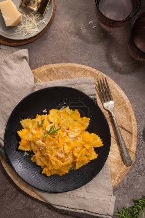 Farfalle pasta with pumpkin sauce and parmesan cheese decorated with rosemary on a black ceramic plate. Creamy cheesy vegan pumpkin pasta. Kitchen counter top. Top view. Flat lay