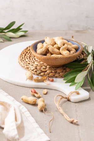 Photo for Peanuts with shell, dry roasted and unshelled peanuts as healthy snack in ceramic bowl in kitchen countertop. For healthy food and diet concepts. - Royalty Free Image