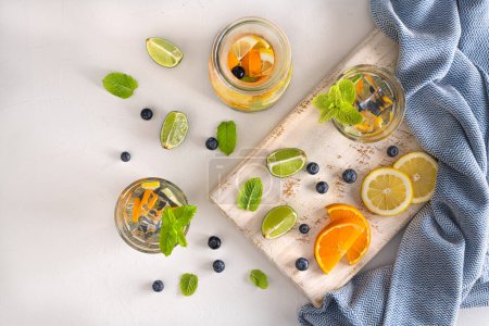 Photo for Summer healthy cocktails of citrus infused waters, lemonades or mojitos, with lime lemon orange blueberries and mint, diet detox beverages, in glasses on light background - Royalty Free Image