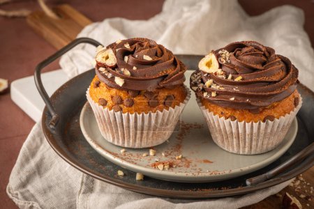 Téléchargez les photos : Muffins aux pépites de chocolat décorés de ganache au chocolat et noisette sur un comptoir de cuisine. - en image libre de droit