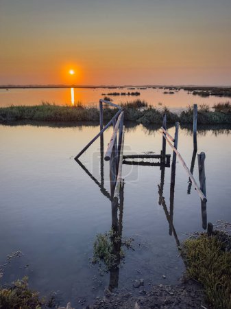 Photo for Old wooden pier at the Ria de Aveiro in Portugal, with calm water at sunset. Murtosa, Portugal. - Royalty Free Image