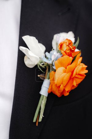 Foto de Boutonniere de boda con flores blancas y rojas en chaqueta negra masculina - Imagen libre de derechos