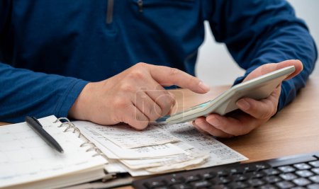 Ein Mann schreibt ein Haushaltsbuch, während er Quittungen organisiert. Eine Nahaufnahme der Hände. Steuer- oder Jahresabrechnungskonzept.
