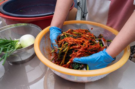 Téléchargez les photos : Le processus de fabrication d'un plat traditionnel coréen, le kimchi. Une femme portant des gants prépare divers ingrédients nécessaires pour le kimchi. - en image libre de droit