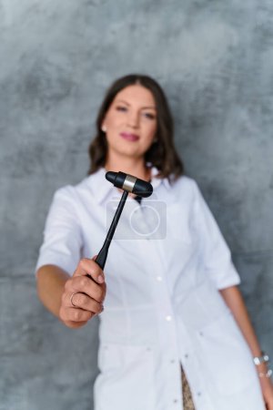 Photo for Doctor woman in a white coat holds a hammer for reflexes in her hands. Focus on the subject. Blurred background - Royalty Free Image