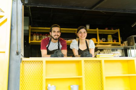 Fröhlicher lateinamerikanischer Koch und Koch, der lächelnd in die Kamera blickt, während er am Fast-Food-Truck arbeitet