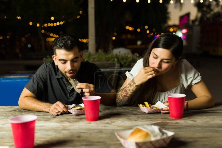 Attractive young man and woman friends coming to the mexican food cart at night and eating delicious tacos