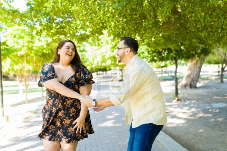 Cheerful caucasian boyfriend and fat girlfriend dancing together and having fun during a date outdoors 