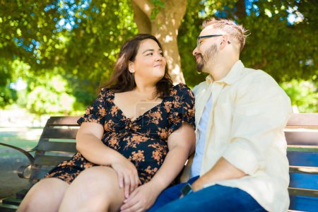 Foto de Adorable pareja feliz relajándose al aire libre durante una cita sentada en el parque del banco - Imagen libre de derechos