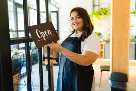 Foto de Retrato de una mujer empresaria sonriendo mientras pone un cartel abierto en su restaurante o cafetería - Imagen libre de derechos