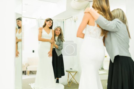 Photo for Happy mother and young woman seen from behind looking in the mirror while buying a wedding gown - Royalty Free Image