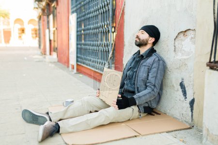 Pauvre mendiant de la rue assis sur un carton par terre et tenant une pancarte demandant de l'aide pour acheter de la nourriture 