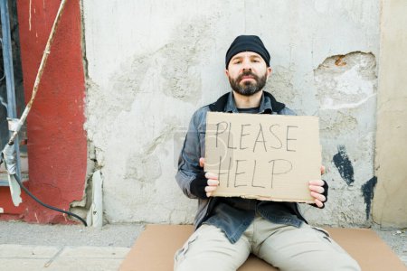 Téléchargez les photos : Portrait d'un misérable sans-abri vivant dans la rue montrant un chant en carton demandant de l'aide pour se nourrir ou de l'argent - en image libre de droit