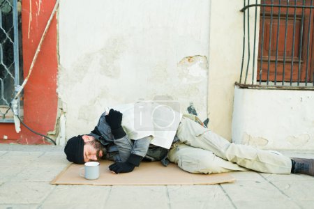 Photo for Miserable homeless man feeling cold living and sleeping on a carbord on the street looking miserable - Royalty Free Image
