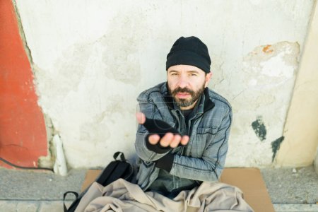 Foto de Hombre hambriento y frío sin hogar mirando a la cámara rogando dinero mientras vive solo en las calles - Imagen libre de derechos