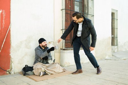 Téléchargez les photos : Homme caucasien donnant de l'argent pour de la nourriture à un mendiant sans abri assis sur du carton dans la rue - en image libre de droit