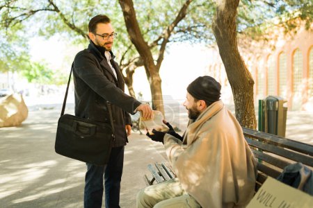 Photo for Happy caucasian man spreading kindness and giving food to a hungry miserable homeless man - Royalty Free Image