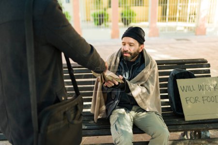 Foto de Pobre hombre hambriento sintiendo frío recibiendo comida de un extraño mientras lucha por vivir en la calle - Imagen libre de derechos