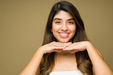 Téléchargez les photos : Superbe jeune femme hispanique montrant sa peau claire et lisse, ses dents blanches et son beau sourire à côté de l'arrière-plan de l'espace de copie - en image libre de droit
