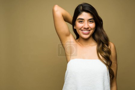 Foto de Mujer joven emocionada usando una toalla que parece feliz mostrando sus axilas después de hacer un procedimiento de depilación contra un fondo con espacio para copiar - Imagen libre de derechos