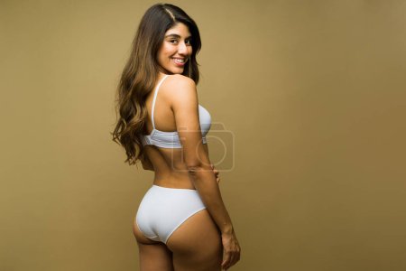 Lächelnde lateinamerikanische Frau von hinten mit einem schönen Körper, der lächelt, während er weiße Unterwäsche trägt 