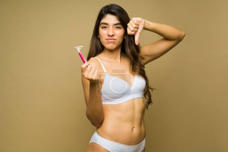 Photo for Sad upset woman looking angry making a thumbs down about using a razor to shave her body - Royalty Free Image