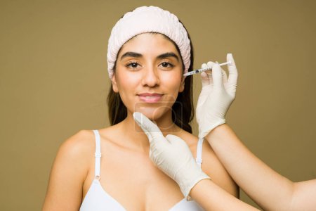 Foto de Mujer feliz recibiendo un lifting facial con inyecciones de toxina botulínica o ácido hialurónico con una jeringa para un procedimiento cosmético - Imagen libre de derechos